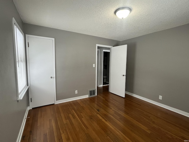 unfurnished bedroom with baseboards, multiple windows, visible vents, and dark wood-style flooring