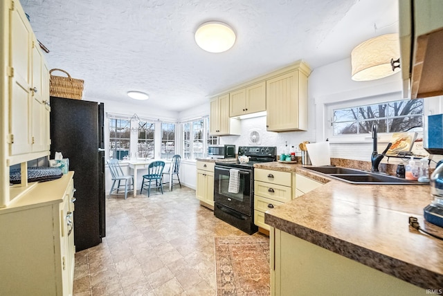 kitchen with a textured ceiling, cream cabinets, a sink, black appliances, and tasteful backsplash