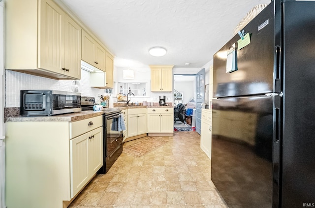 kitchen with tasteful backsplash, light countertops, cream cabinetry, black appliances, and a sink