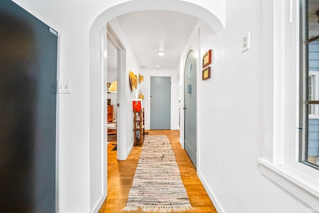 corridor with arched walkways, light wood-style flooring, and baseboards