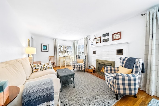 living area featuring a brick fireplace, visible vents, and light wood-style floors