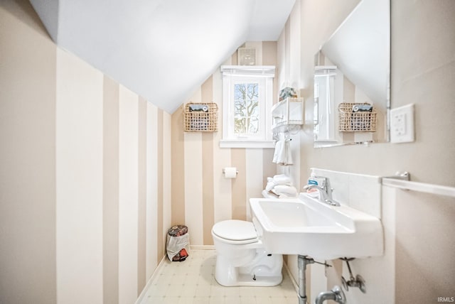 bathroom featuring lofted ceiling, toilet, a sink, baseboards, and tile patterned floors