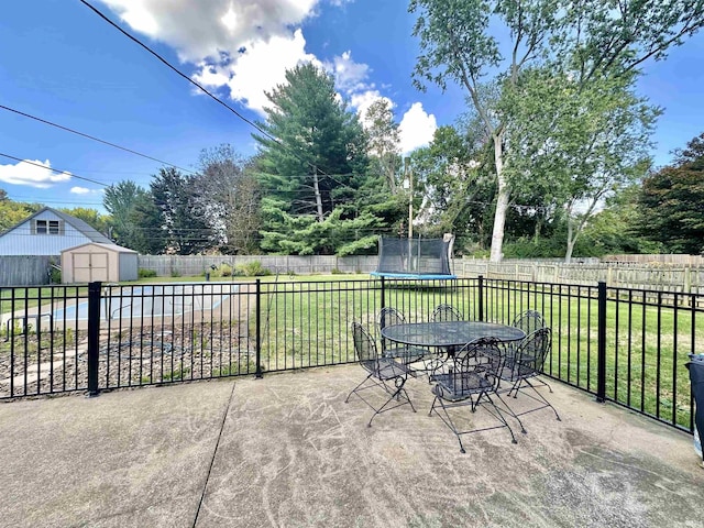 view of patio with a fenced backyard, a trampoline, an outdoor structure, a shed, and outdoor dining space