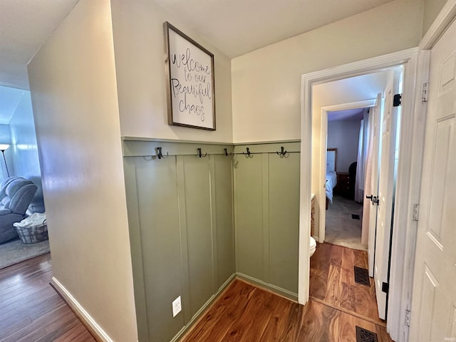 hallway with dark wood-style floors, wainscoting, visible vents, and a decorative wall