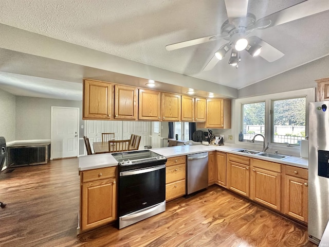 kitchen with a peninsula, a sink, light countertops, appliances with stainless steel finishes, and light wood finished floors