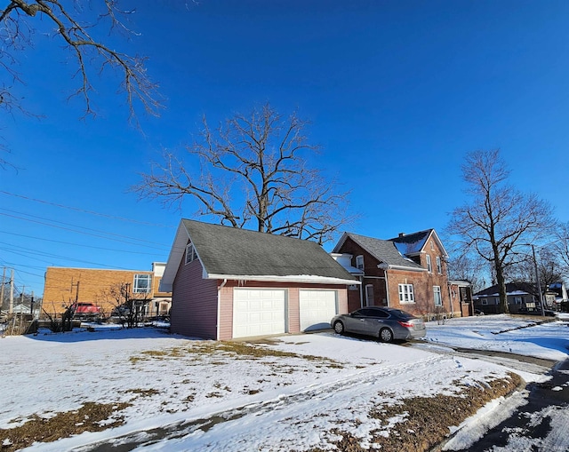 view of snow covered exterior featuring a detached garage and an outbuilding