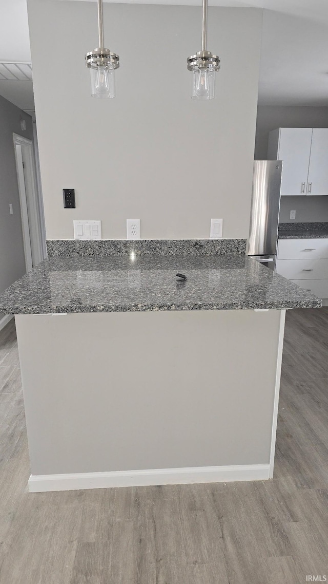 kitchen featuring freestanding refrigerator, dark stone countertops, decorative light fixtures, and white cabinets