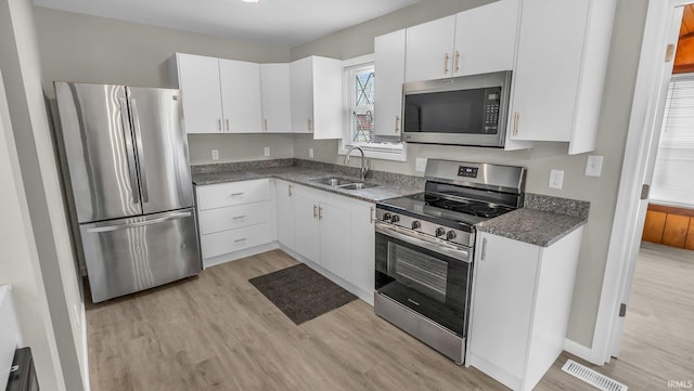 kitchen with dark countertops, white cabinetry, appliances with stainless steel finishes, and a sink