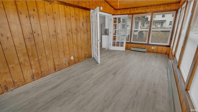 spare room with wooden walls, a sunroom, light wood-style floors, vaulted ceiling, and baseboard heating