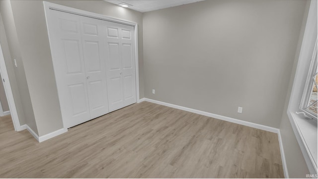 unfurnished bedroom with a closet, light wood-style flooring, and baseboards