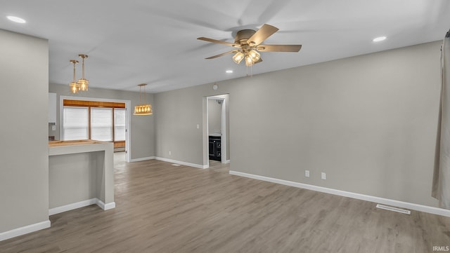 unfurnished living room with a ceiling fan, light wood-type flooring, visible vents, and baseboards