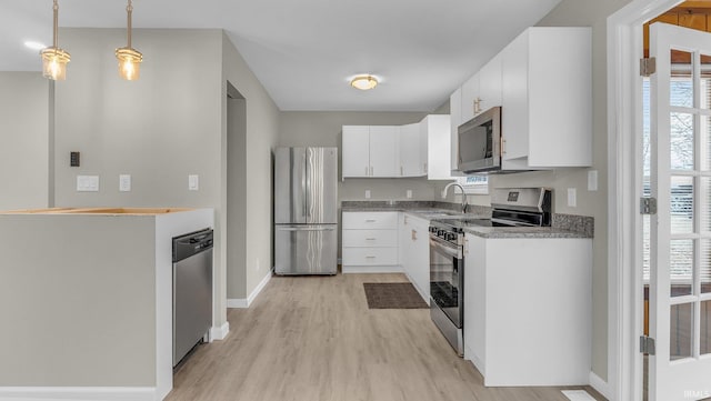 kitchen featuring light wood finished floors, appliances with stainless steel finishes, decorative light fixtures, white cabinetry, and a sink