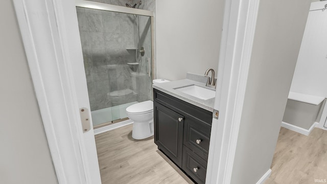 bathroom with toilet, wood finished floors, vanity, baseboards, and a shower stall