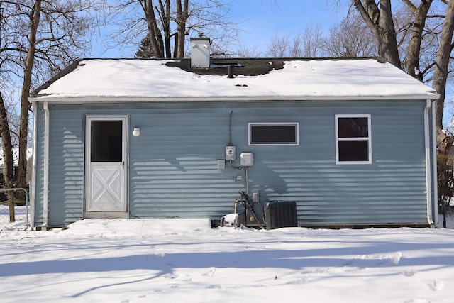 snow covered house featuring a chimney and cooling unit