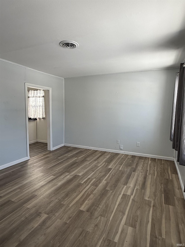 empty room with dark wood-style floors, visible vents, and baseboards