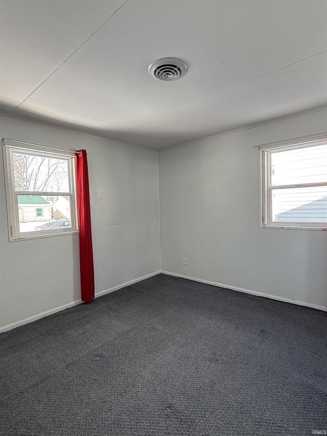 empty room with dark carpet, visible vents, and baseboards