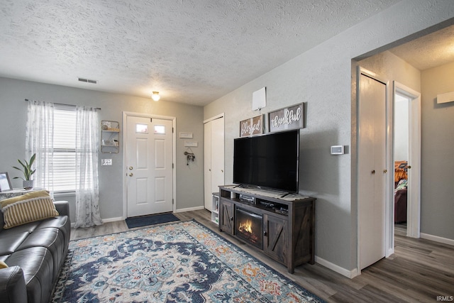 living room featuring baseboards, visible vents, a textured wall, wood finished floors, and a textured ceiling