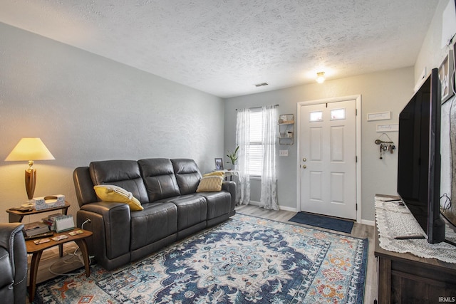 living area featuring a textured ceiling, a textured wall, wood finished floors, visible vents, and baseboards