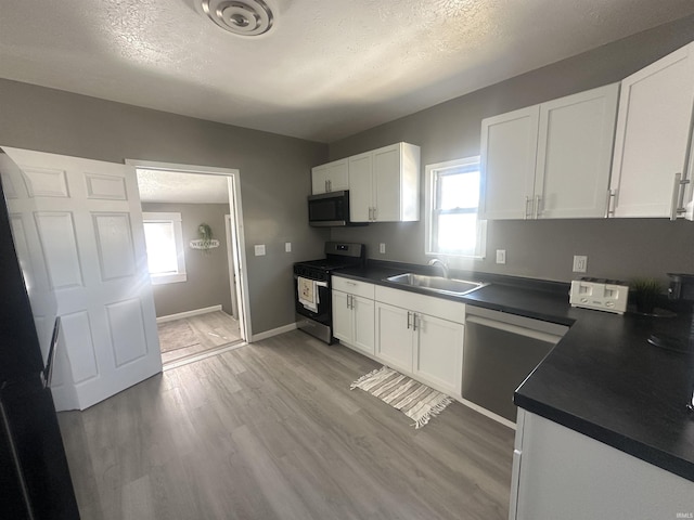 kitchen with dark countertops, appliances with stainless steel finishes, white cabinets, and a sink