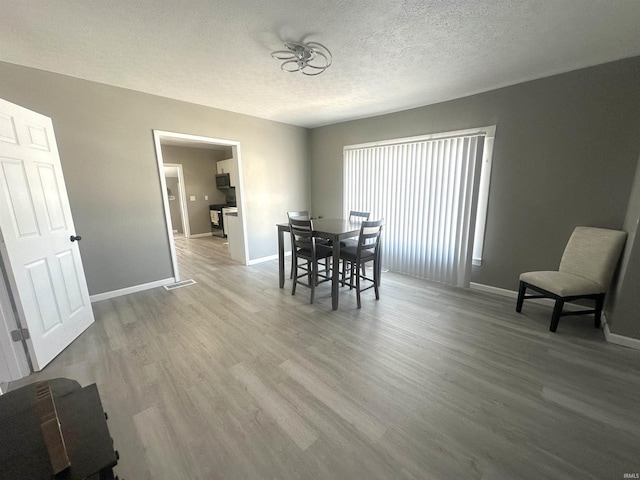 dining space with visible vents, a textured ceiling, baseboards, and wood finished floors