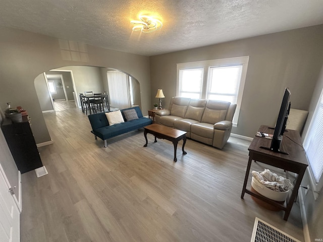 living room with baseboards, visible vents, arched walkways, a textured ceiling, and light wood-type flooring