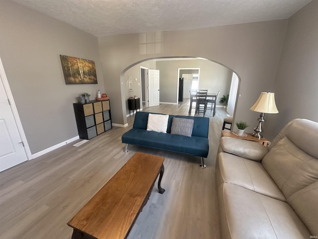 living area featuring baseboards, a textured ceiling, arched walkways, and wood finished floors