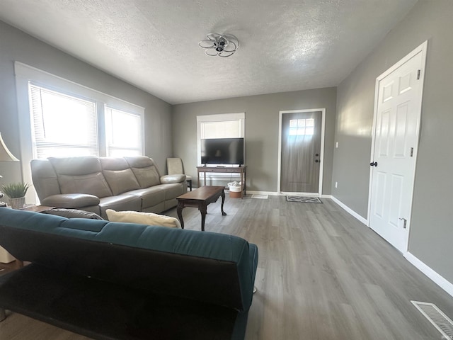 living area with a textured ceiling, light wood-type flooring, visible vents, and baseboards