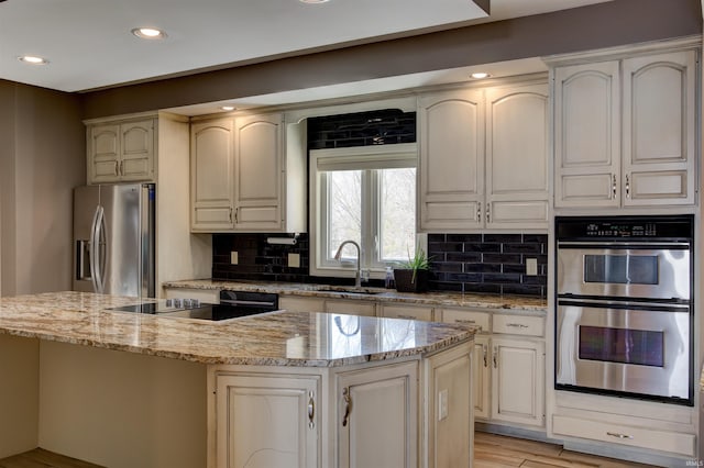 kitchen featuring a sink, a kitchen island, appliances with stainless steel finishes, light stone countertops, and tasteful backsplash