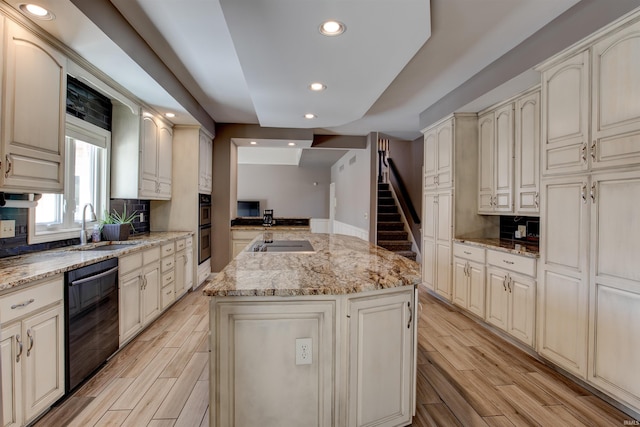 kitchen featuring wood finish floors, a sink, a kitchen island, light stone countertops, and black appliances