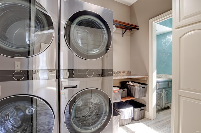 clothes washing area with laundry area, light wood-style flooring, and stacked washer and clothes dryer