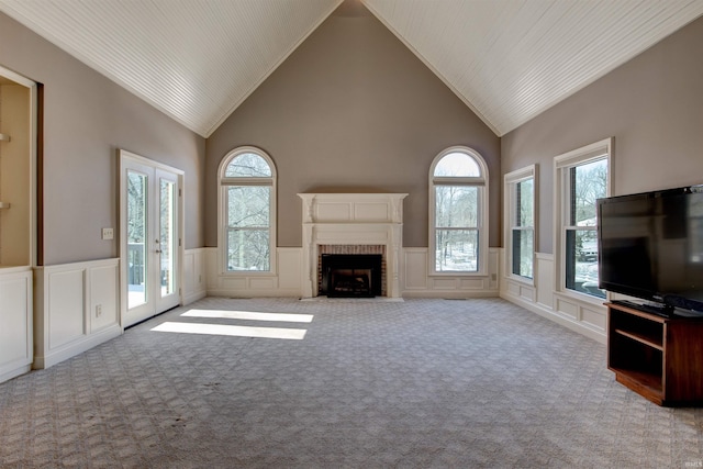 unfurnished living room featuring light carpet, a wainscoted wall, french doors, a fireplace, and high vaulted ceiling