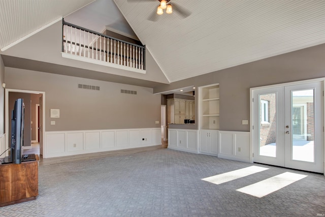 unfurnished living room with built in shelves, french doors, a wainscoted wall, visible vents, and a decorative wall