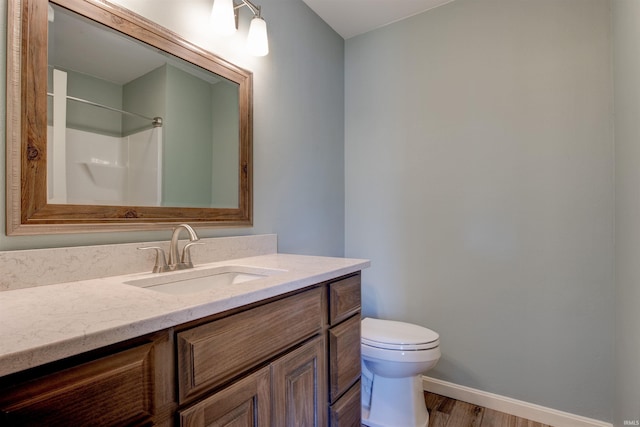 bathroom with toilet, wood finished floors, vanity, baseboards, and walk in shower