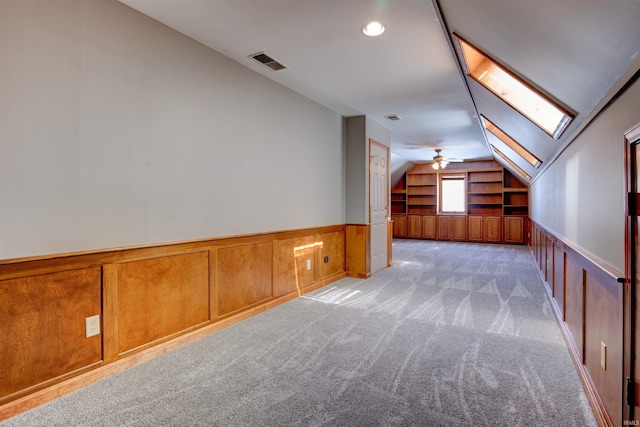 additional living space featuring light colored carpet, a wainscoted wall, visible vents, built in features, and lofted ceiling with skylight