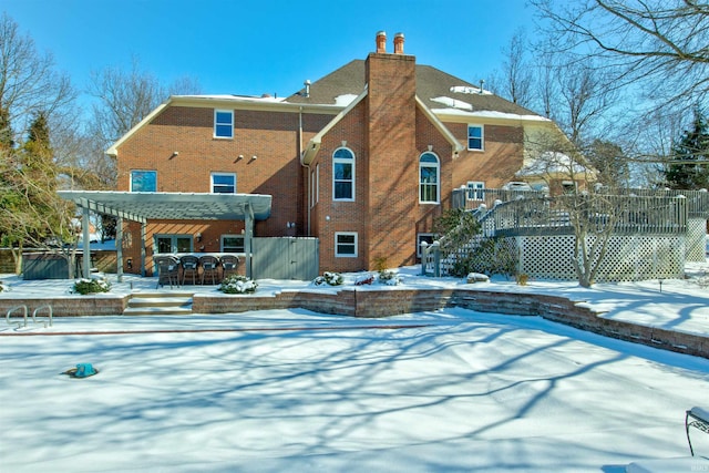 snow covered rear of property with a chimney, stairway, a wooden deck, a pergola, and brick siding