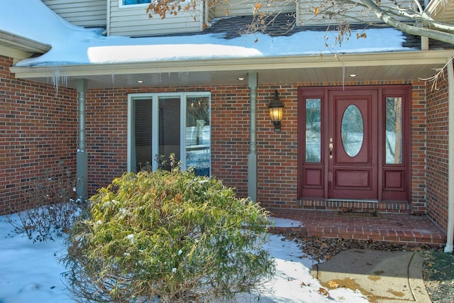 snow covered property entrance featuring brick siding