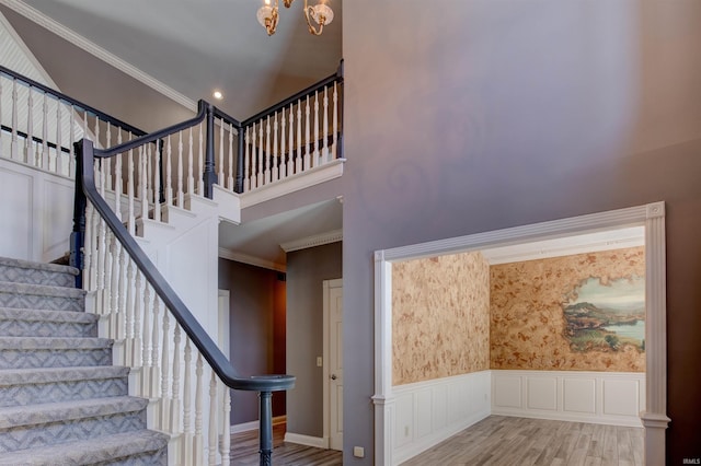 stairway featuring a decorative wall, wood finished floors, a towering ceiling, ornamental molding, and wainscoting