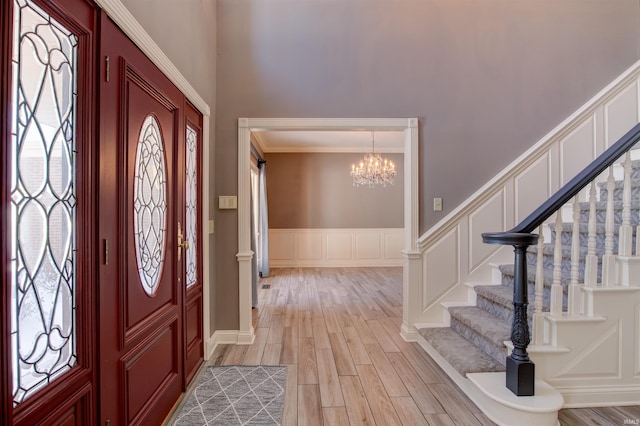 entrance foyer with light wood finished floors, a decorative wall, stairway, wainscoting, and a chandelier