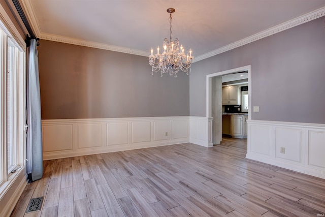 spare room featuring light wood finished floors, visible vents, crown molding, and an inviting chandelier