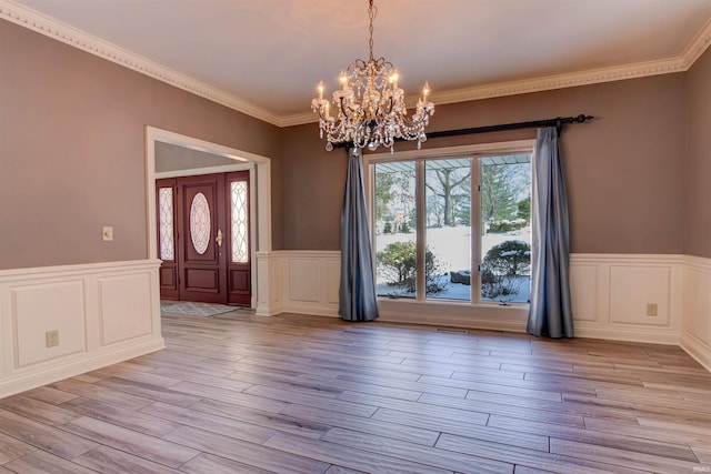 foyer with visible vents, light wood-style floors, ornamental molding, wainscoting, and an inviting chandelier