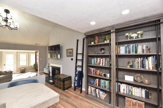 interior space with wood finished floors, vaulted ceiling, a textured ceiling, a fireplace, and a notable chandelier