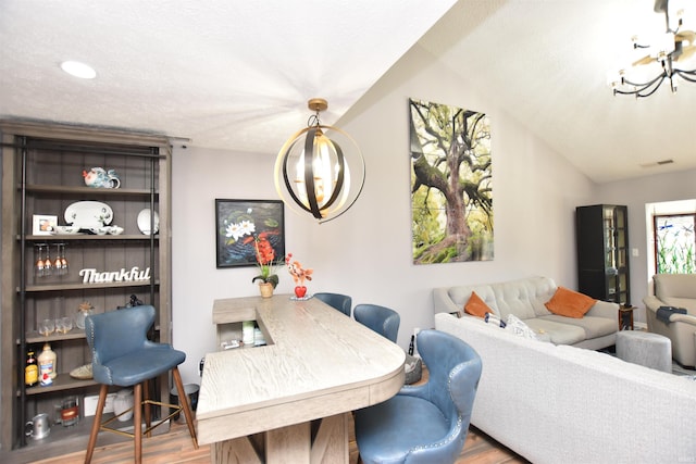 dining space with a chandelier, lofted ceiling, visible vents, and wood finished floors