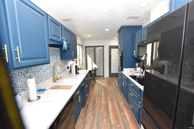 kitchen featuring black appliances, blue cabinetry, light countertops, and a sink