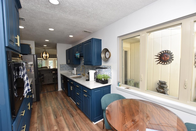 kitchen with decorative backsplash, dark wood-type flooring, light countertops, blue cabinetry, and a sink