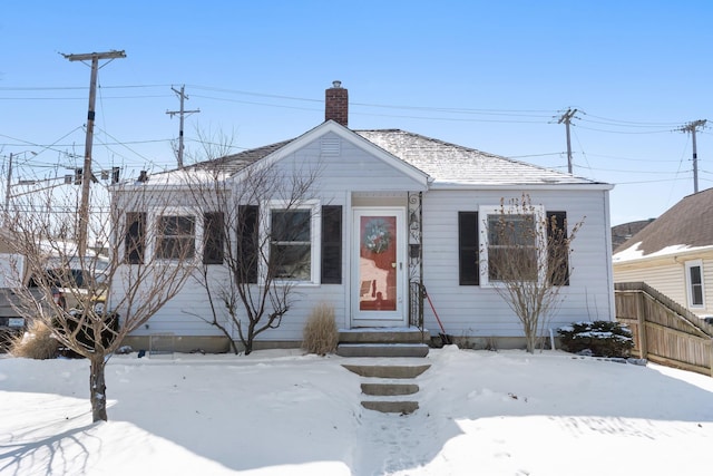 bungalow-style home featuring entry steps, a chimney, fence, and roof with shingles