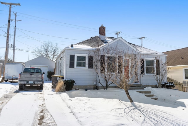 bungalow-style house with roof with shingles, a chimney, a detached garage, and an outdoor structure