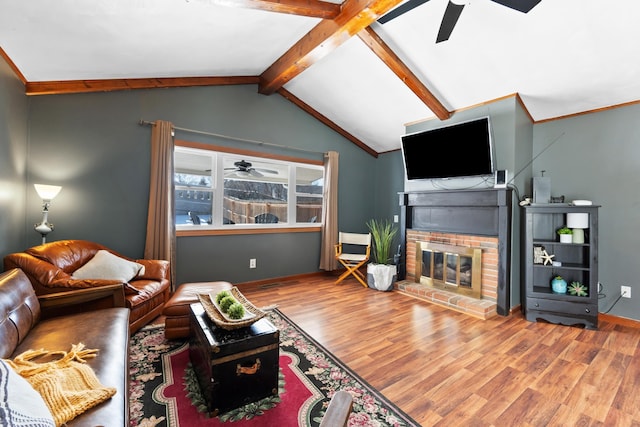 living room with lofted ceiling with beams, wood finished floors, a ceiling fan, baseboards, and a brick fireplace