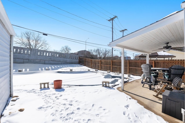 snowy yard with a fenced backyard and a ceiling fan