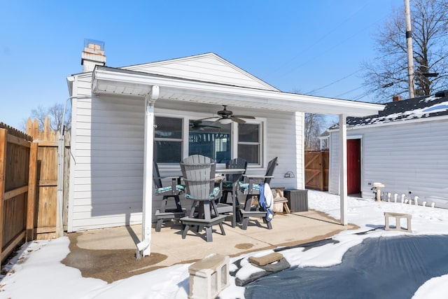 snow covered patio featuring ceiling fan and fence