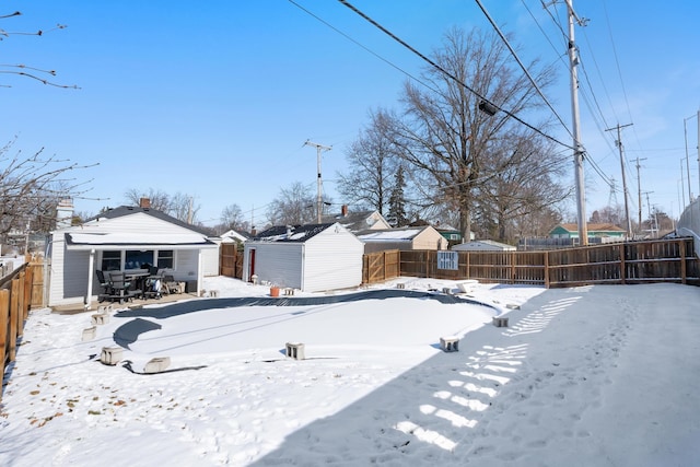 yard covered in snow featuring a storage unit, an outdoor structure, a fenced backyard, and a detached garage